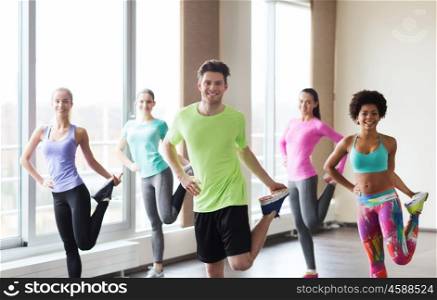 fitness, sport, training, gym and lifestyle concept - group of smiling people with trainer exercising and stretching in gym. group of smiling people exercising in gym
