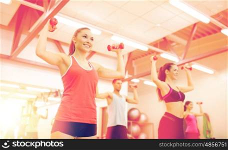 fitness, sport, training, gym and lifestyle concept - group of smiling people working out with dumbbells in the gym