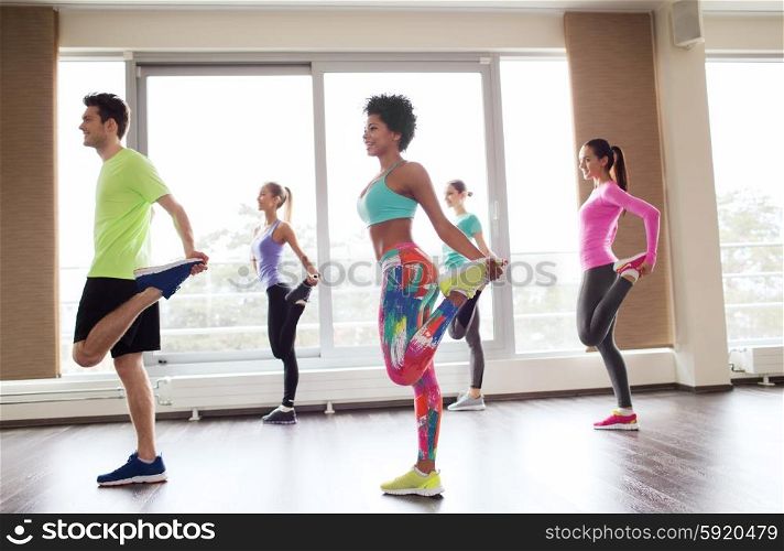 fitness, sport, training, gym and lifestyle concept - group of smiling people with trainer exercising and stretching in gym