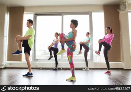 fitness, sport, training, gym and lifestyle concept - group of smiling people with trainer exercising and stretching in gym
