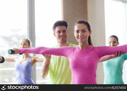 fitness, sport, training, gym and lifestyle concept - group of smiling people working out with dumbbells flexing muscles s in gym