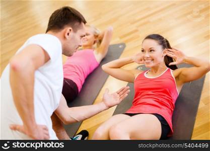 fitness, sport, training, gym and lifestyle concept - group of smiling women with male trainer doing sit ups on mats in the gym