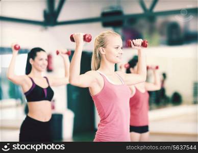 fitness, sport, training, gym and lifestyle concept - group of smiling women working out with dumbbells in the gym