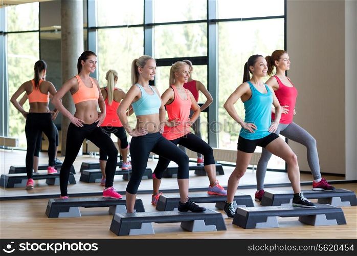 fitness, sport, training, gym and lifestyle concept - group of women working out with steppers in gym