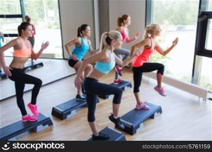 fitness, sport, training, gym and lifestyle concept - group of women working out with steppers in gym