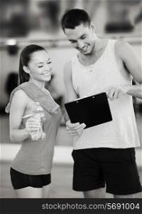fitness, sport, training, gym and lifestyle concept - smiling male trainer with clipboard and woman with water bottle in the gym