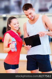 fitness, sport, training, gym and lifestyle concept - smiling male trainer with clipboard and woman with water bottle in the gym