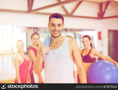 fitness, sport, training, gym and lifestyle concept - smiling man standing in front of the group of people in gym. smiling man standing in front of the group in gym