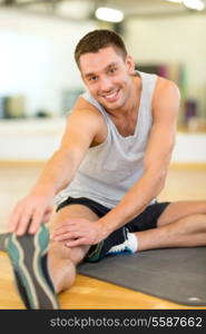 fitness, sport, training, gym and lifestyle concept - smiling man stretching on mat in the gym