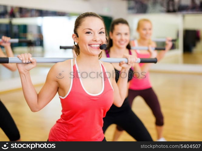 fitness, sport, training, gym and lifestyle concept - smiling trainer in front of the group of people working out with barbells in the gym