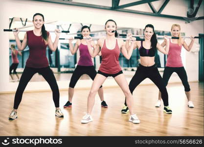 fitness, sport, training, gym and lifestyle concept - smiling trainer in front of the group of people working out with barbells in the gym