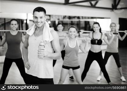 fitness, sport, training, gym and lifestyle concept - smiling trainer in front of group of people working out with barbells in the gym