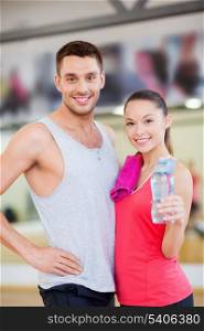 fitness, sport, training, gym and lifestyle concept - smiling woman and man in the gym with water bottle and towel after class