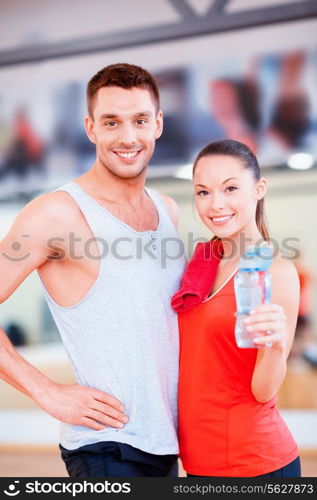 fitness, sport, training, gym and lifestyle concept - smiling woman and man in the gym with water bottle and towel after class