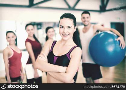 fitness, sport, training, gym and lifestyle concept - smiling woman standing in front of the group of people in gym