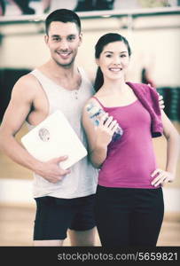 fitness, sport, training, gym and lifestyle concept - two smiling people with scale and water bottle in the gym