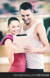 fitness, sport, training, gym and lifestyle concept - two smiling people with tablet pc in the gym