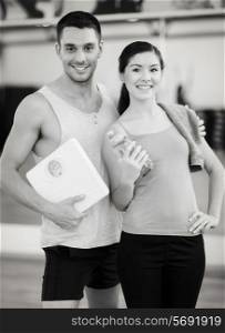 fitness, sport, training, gym and lifestyle concept - two smiling people with scale and water bottle in the gym