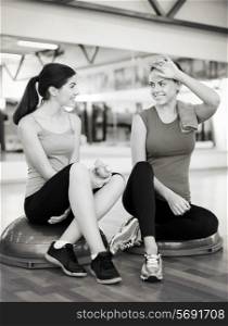 fitness, sport, training, gym and lifestyle concept - two smiling women sitting on the half ball and relaxing after class in the gym