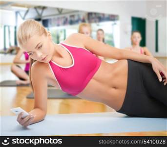 fitness, sport, training, gym and lifestyle concept - woman lying on the floor and looking into smartphone in the gym