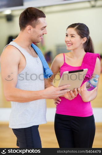 fitness, sport, training, gym, technology and lifestyle concept - two smiling people with tablet pc computer and water bottle in the gym