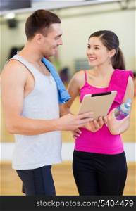 fitness, sport, training, gym, technology and lifestyle concept - two smiling people with tablet pc computer and water bottle in the gym
