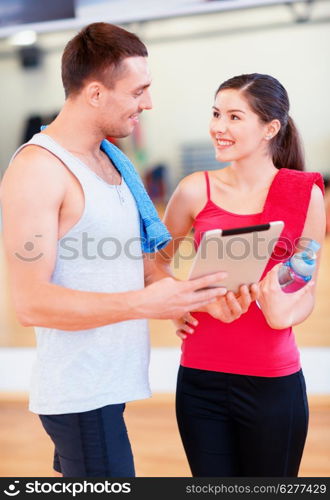 fitness, sport, training, gym, technology and lifestyle concept - two smiling people with tablet pc computer and water bottle in the gym