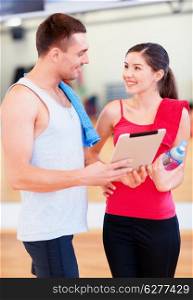 fitness, sport, training, gym, technology and lifestyle concept - two smiling people with tablet pc computer and water bottle in the gym