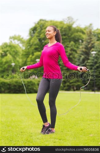 fitness, sport, training, park and lifestyle concept - smiling african american woman exercising with jump-rope outdoors