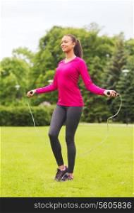 fitness, sport, training, park and lifestyle concept - smiling african american woman exercising with jump-rope outdoors