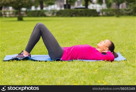 fitness, sport, training, park and lifestyle concept - smiling woman doing exercises on mat outdoors