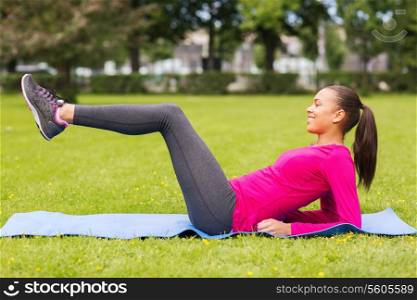 fitness, sport, training, park and lifestyle concept - smiling woman doing exercises on mat outdoors