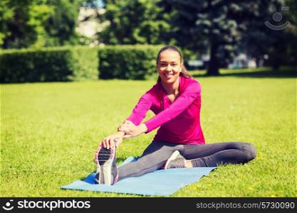 fitness, sport, training, park and lifestyle concept - smiling woman stretching leg on mat outdoors