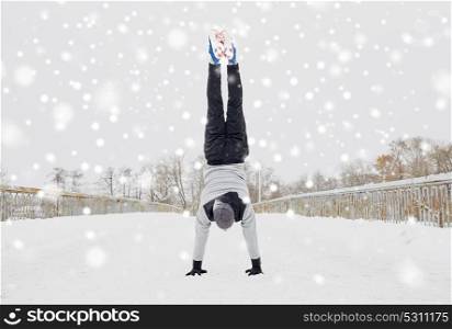 fitness, sport, training, people and exercising concept - young man on doing handstand outdoors in winter. young man doing handstand in winter