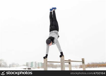 fitness, sport, training, people and exercising concept - young man on parallel bars doing handstand outdoors in winter