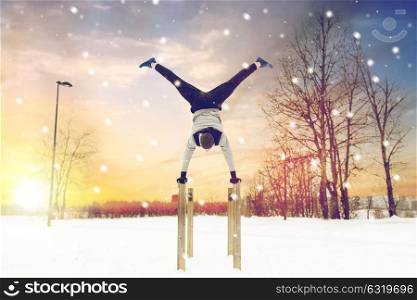 fitness, sport, training, people and exercising concept - young man on parallel bars doing handstand outdoors in winter. young man exercising on parallel bars in winter