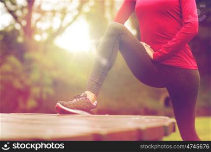 fitness, sport, training, people and lifestyle concept - close up of woman stretching leg and doing lunge on bench in park. close up of woman stretching leg outdoors