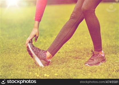 fitness, sport, training, people and lifestyle concept - close up of woman stretching leg in park