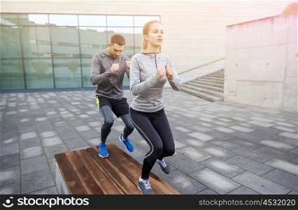 fitness, sport, training, people and lifestyle concept - couple making step exercise on city street bench