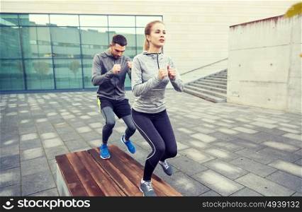 fitness, sport, training, people and lifestyle concept - couple making step exercise on city street bench. couple making step exercise on city street bench