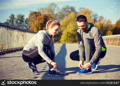 fitness, sport, training, people and lifestyle concept - smiling couple tying shoelaces of sneakers outdoors. smiling couple tying shoelaces outdoors