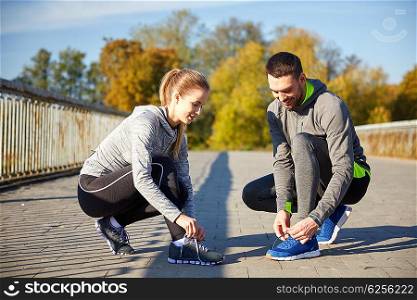fitness, sport, training, people and lifestyle concept - smiling couple tying shoelaces of sneakers outdoors