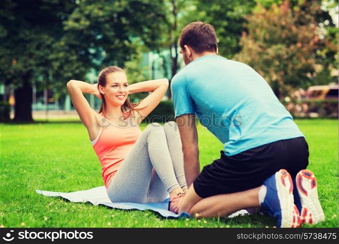 fitness, sport, training, teamwork and lifestyle concept - smiling woman with personal trainer doing exercises on mat outdoors