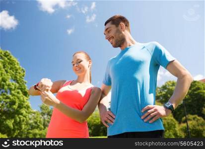 fitness, sport, training, technology and lifestyle concept - two smiling people with heart rate watches outdoors