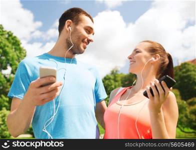 fitness, sport, training, technology and lifestyle concept - two smiling people with smartphones and earphones outdoors