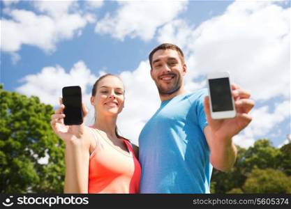 fitness, sport, training, technology and lifestyle concept - two smiling people with smartphones outdoors