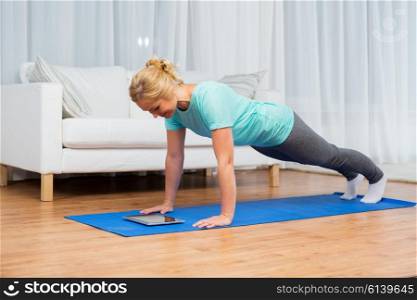fitness, sport, training, technology and people concept - happy woman with tablet pc computer doing plank exercise on mat at home
