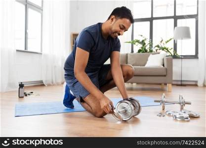 fitness, sport, weightlifting and bodybuilding concept - smiling indian man assembling dumbbells at home. smiling indian man assembling dumbbells at home