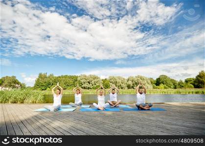 fitness, sport, yoga and healthy lifestyle concept - close up of people meditating in easy sitting pose on river or lake berth