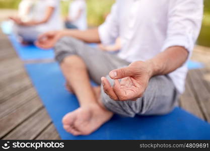 fitness, sport, yoga and healthy lifestyle concept - close up of people meditating in easy sitting pose on river or lake berth